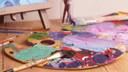Artist's palette with mixed bright paints and brush on wooden table