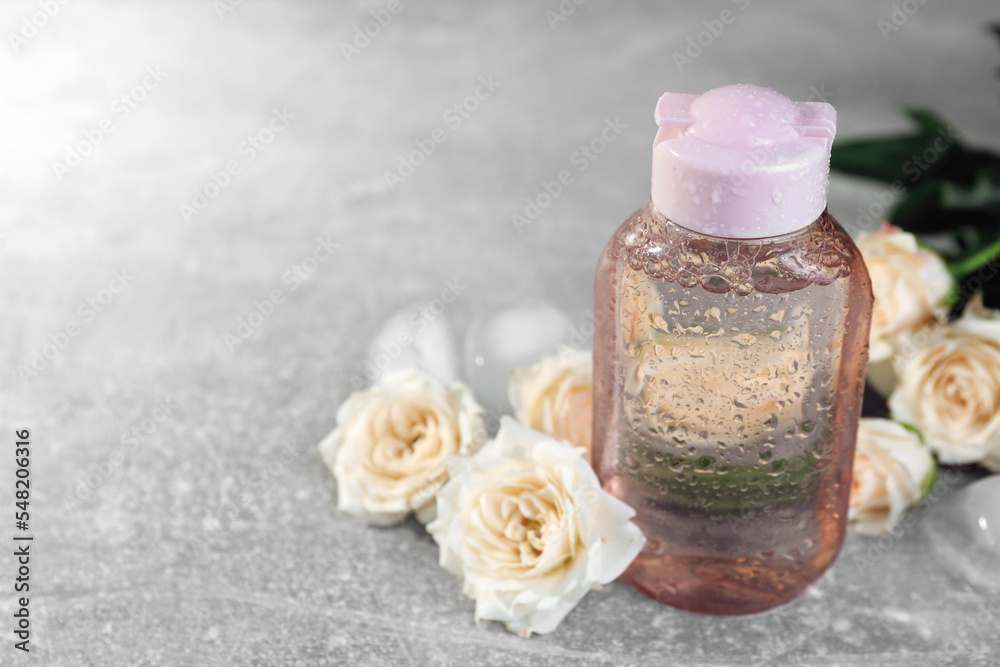 Micellar water and roses on grey table, closeup. Space for text