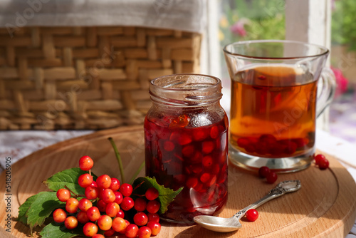 Tasty hot drink, jam and viburnum berries on wooden board indoors