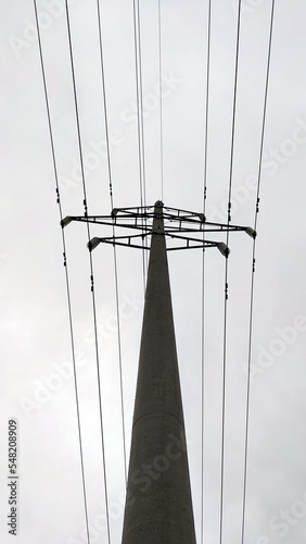 A tall concrete pole with electrical wires. A cement pylon of a power line under a light gray sky that is covered with clouds. Oprah is holding several high voltage metal wires. photo