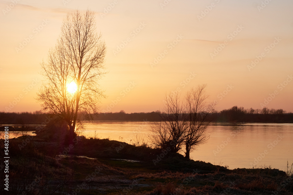 Sunset over the river. Orange sunset through the riverside trees