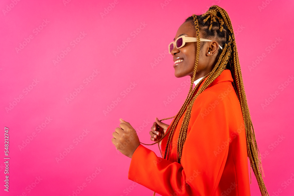African young woman with braids on a pink background, portrait in the studio in a red outfit having fun