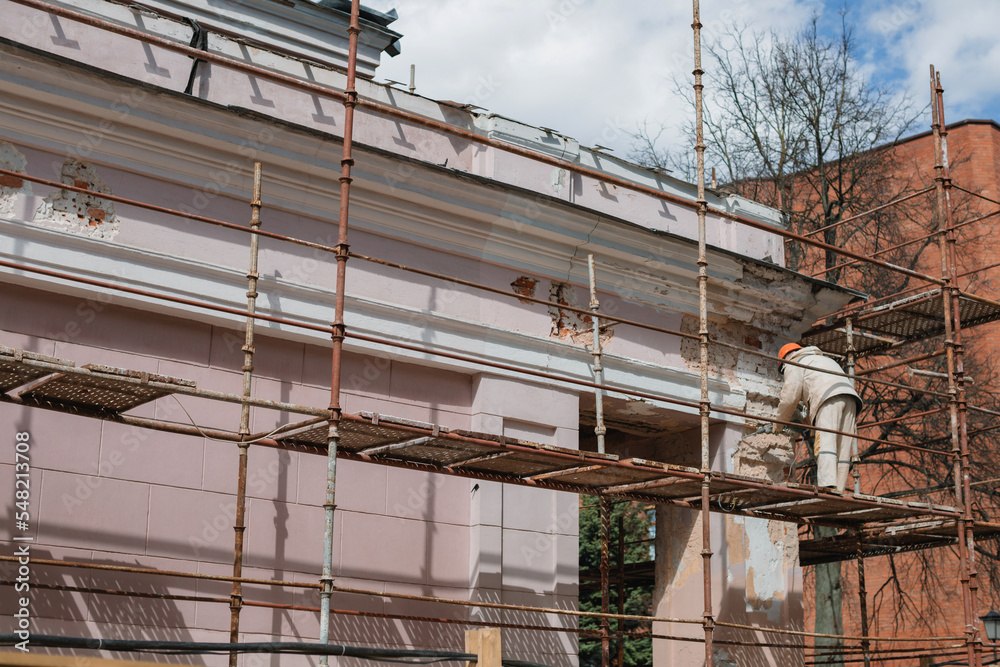 Unrecognizable fragment of a building in scaffolding. Unrecognizable builder repairing the facade. Restoration of the building. Unrecognizable fragment of a building in scaffolding. Unrecognizable builder repairing the facade. Restoration of the building.