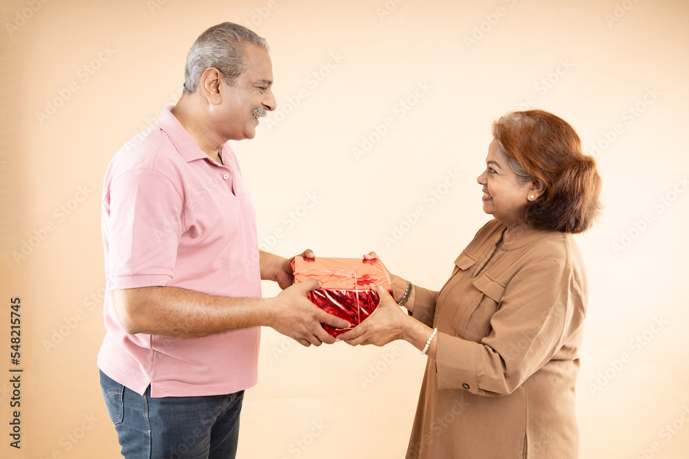 Happy indian senior couple holding gift boxes and celebrating valentine'day together isolated on beige background. Romantic husband give present to his wife to express his love. Happy indian senior couple holding gift boxes and celebrating valentine'day together isolated on beige background. Romantic husband give present to his wife to express his love.