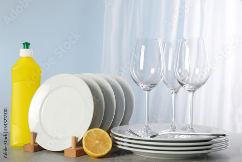 Glasses, clean dishware and bottle of detergent on grey marble table