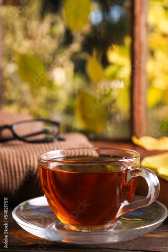 Cup of aromatic tea and soft sweater on wooden windowsill indoors, closeup. Autumn atmosphere