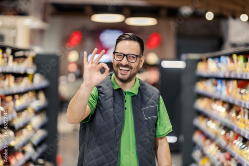 Φωτογραφία A salesman is standing at the marketplace and showing okay gesture at the camera