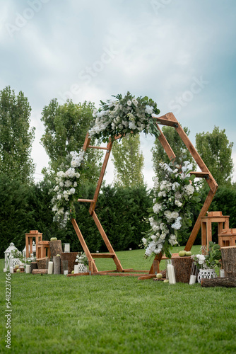Wedding ceremony. Very beautiful and stylish hexagonal wedding arch, decorated with various fresh flowers, standing in the garden.