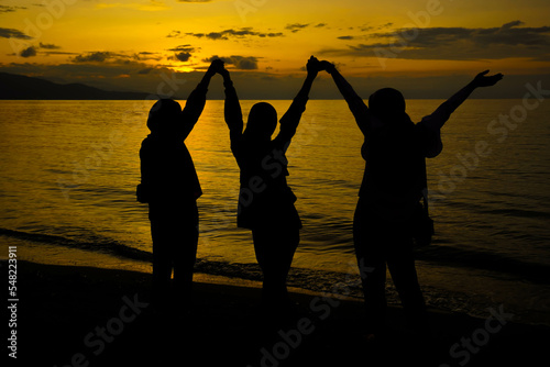 Happy and free Siluet people on sunset background, Silhouette three women with Raised Hands at Sunset photo