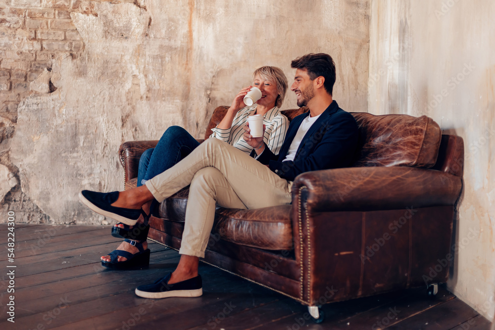 Obraz premium friends talking sitting on sofa - colleagues taking a break at work with a coffee