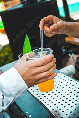 The bartender prepares a cocktail with passion fruit in a plastic glass with a straw