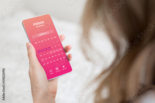 woman holding a mobile phone with a menstrual cycle calendar application photo