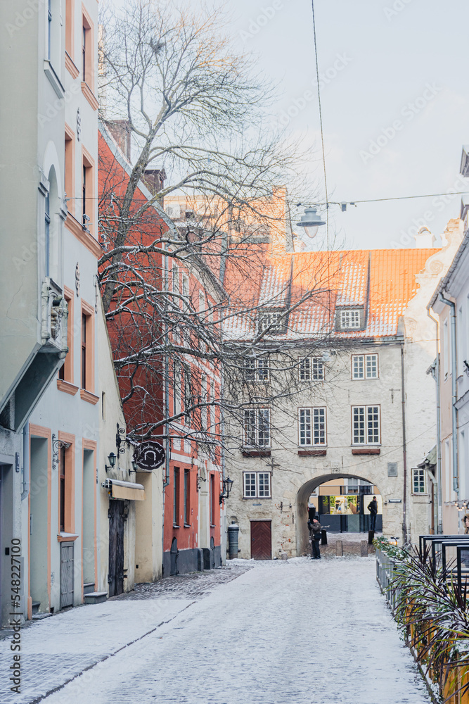Beautiful narrow street with cobblestones in Riga Old Town with houses, buildings and restaurants in winter covered by the snow, vertical 