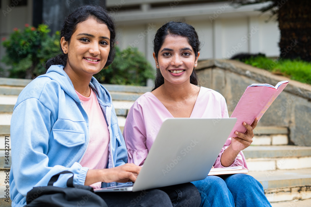 focus on girl with book, Happy College students looking at camera while busy working on laptop on university campus - concept of education, teamwork and friendship