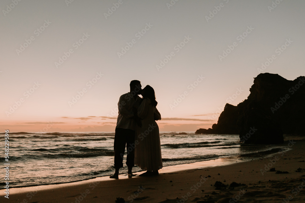 The man holds his pregnant wife's tummy and she holds her tummy too, the couple in love is walking along the small Praia de Paredes da Vitória, enjoying the freshness of the air and their love. The co
