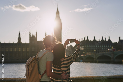 Phone, selfie and couple by the big ben in London on vacation, adventure or holiday together. Travel, building and young tourist man and woman taking a picture on a smartphone in the city in England.