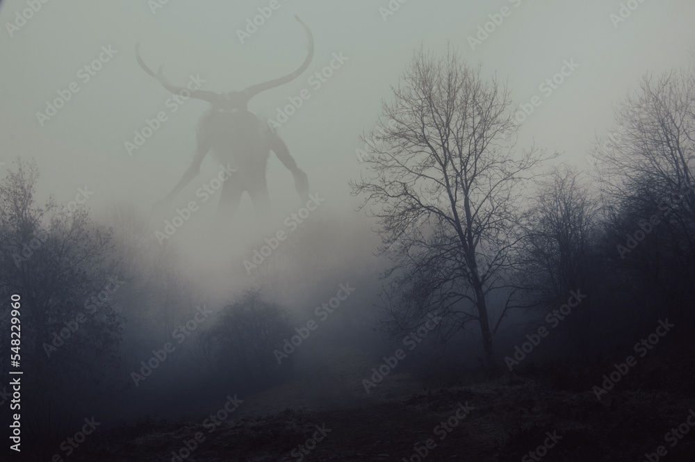 A fantasy concept of a horned god like monster. Looking across a forest on a spooky foggy, winters day.