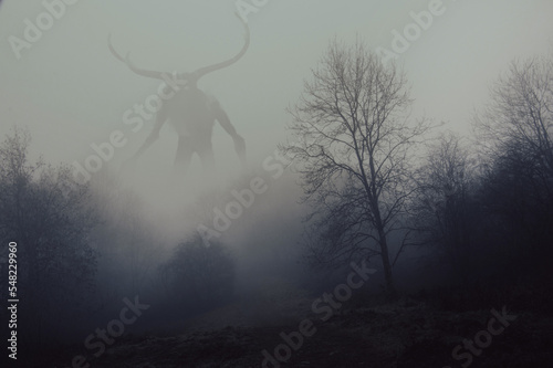 A fantasy concept of a horned god like monster. Looking across a forest on a spooky foggy, winters day.