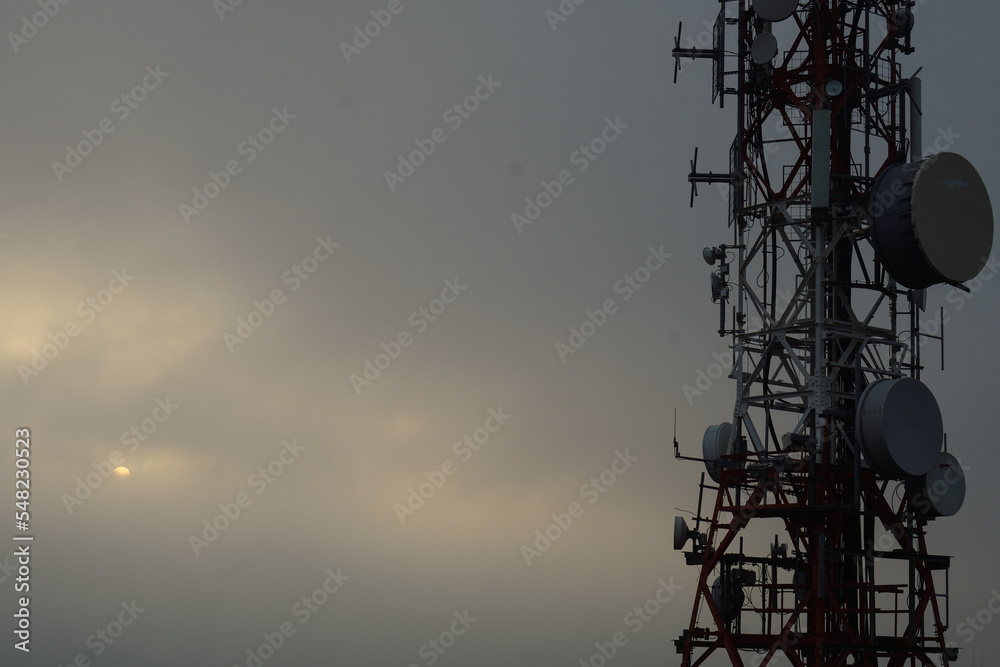 Television and mobile phone antenna at sunset with the sun in the fog Television and mobile phone antenna at sunset with the sun in the fog