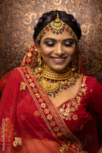 Shy Indian bridal woman Wearing Beautiful makeup dressed in Hindu traditional wedding Red lehenga. jewelry set which consisting necklace and head adornment (maang tikka)