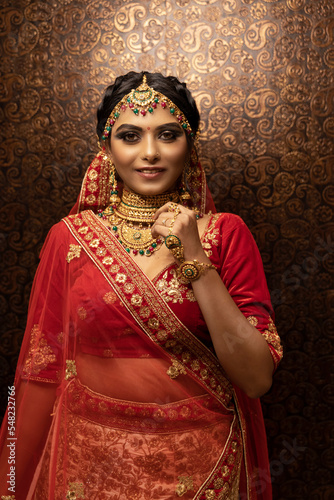 Beautiful Indian bride dressed in Hindu traditional wedding clothes Red lehenga embroidered with heavy jewelry posing for shoot. bridal makeup