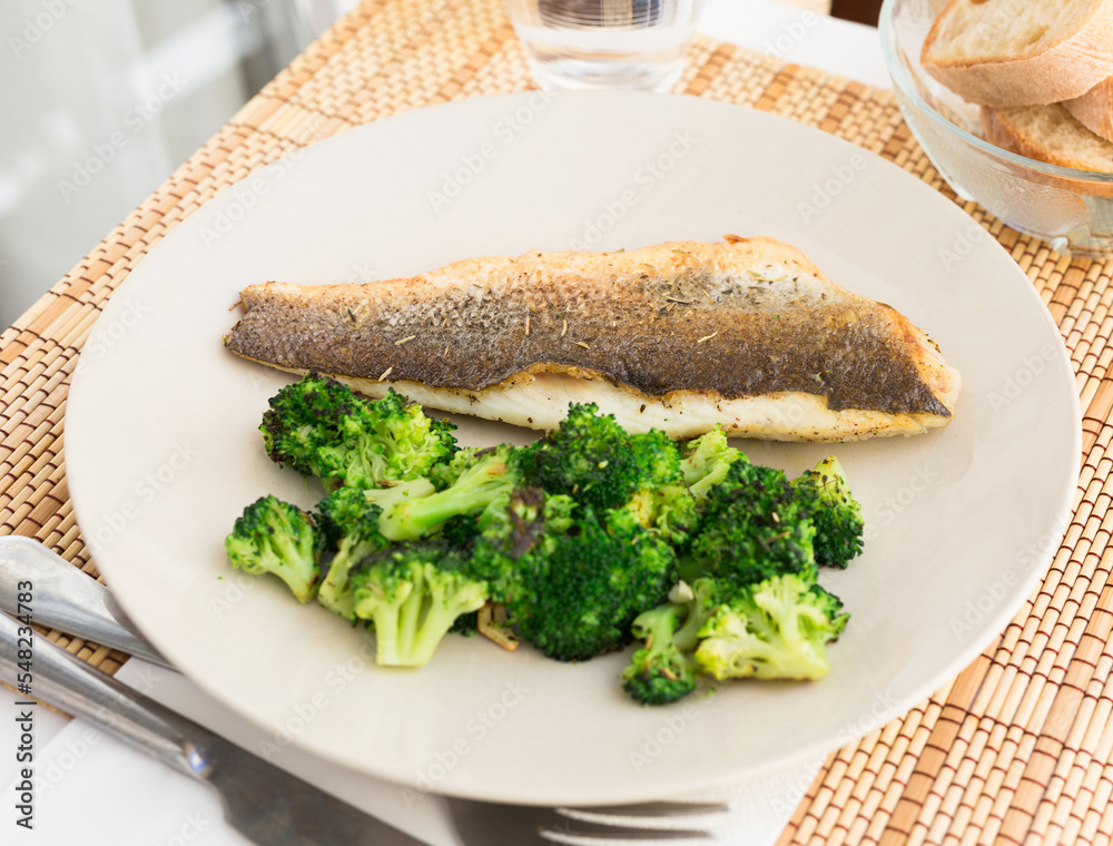 fried fillet of sea bass with garnish of broccoli on black warm stone plate fried fillet of sea bass with garnish of broccoli on black warm stone plate
