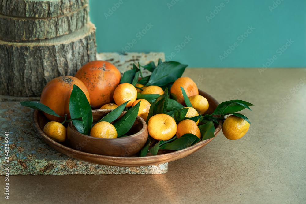 Fresh ripe not perfect small tangerines with leaves lie on a wooden plate. Green fruit background. Concept of imperfect products.