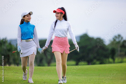 Two young asian professional golfers walking hand in hand and talk like friend and smiling happily on the golf course,