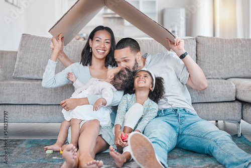 Happy family, cardboard roof or house life insurance in home living room floor in security, mortgage loan success or investment support. Property cover for smile, happy mother or father and children photo