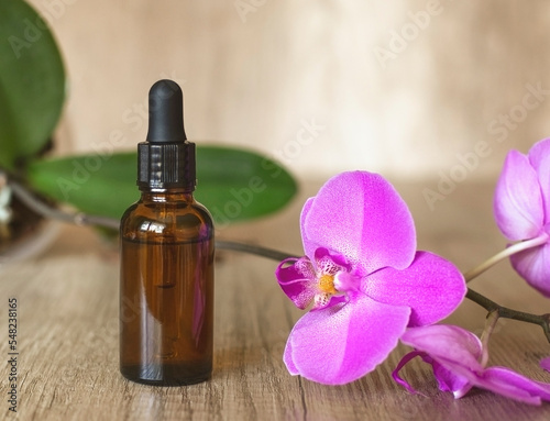 Dark serum bottle with pipette on wooden textured table with a blooming purple orchid