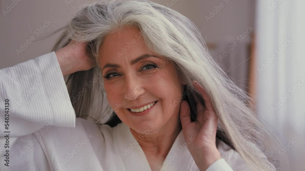 Female portrait close up headshot 60s old middle-aged mature senior aging Caucasian woman grandma senior older 50s lady model with long shiny smooth gray hair smiling looking at camera wind haircare