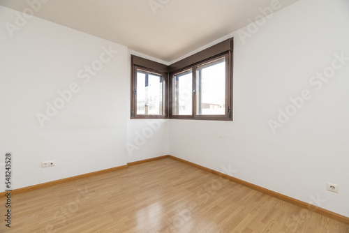 Empty living room with wooden laminate flooring with bare white walls and two brown anodized aluminum corner windows
