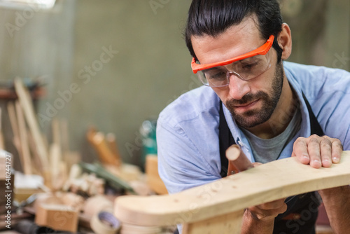 young carpenter man wearing goggles working use sandpaper for wood polishing. factory industry woodwork. craftsman professional technician handmade.