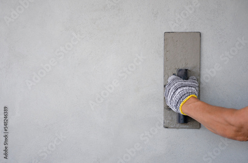 worker hand holding trowel is plastering cement wall