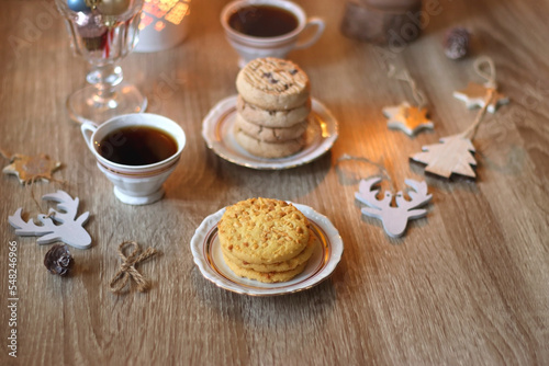 Two types of cookies, cups of tea or coffee, various Christmas decorations and lit candles. Cozy Christmas atmosphere at home. Selective focus.