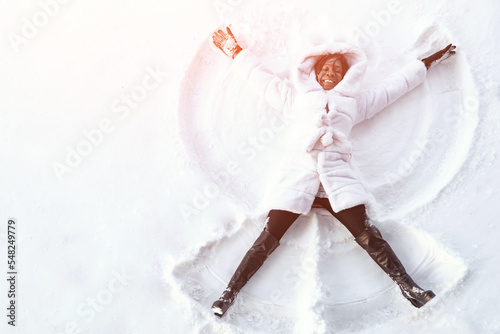 Cuadro en lienzo African smiling woman lies on snow drawing snow angel figure in winter day, sunl