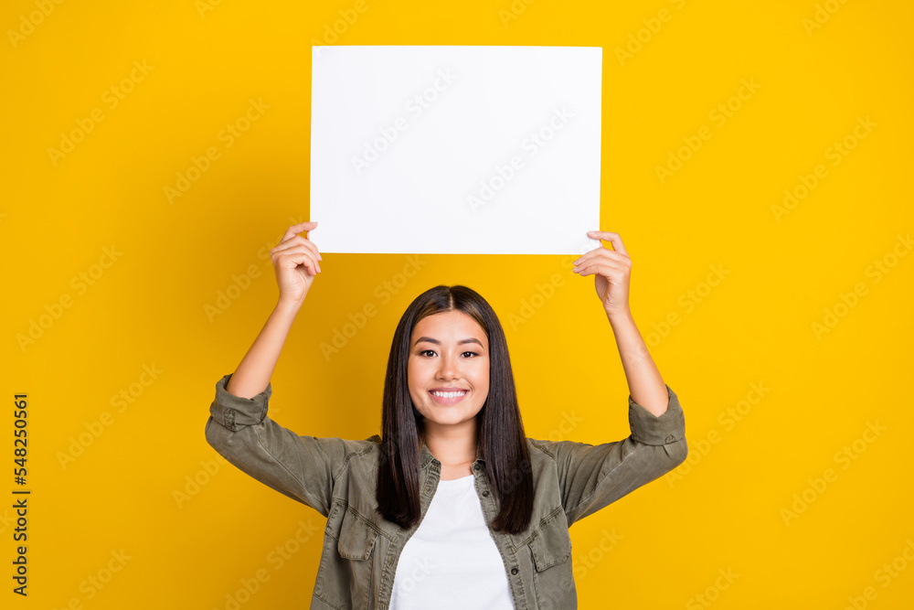 Photo of young cheerful smiling vietnamese lady wear shirt hold white paper empty blank with useful information isolated on yellow color background Photo of young cheerful smiling vietnamese lady wear shirt hold white paper empty blank with useful information isolated on yellow color background