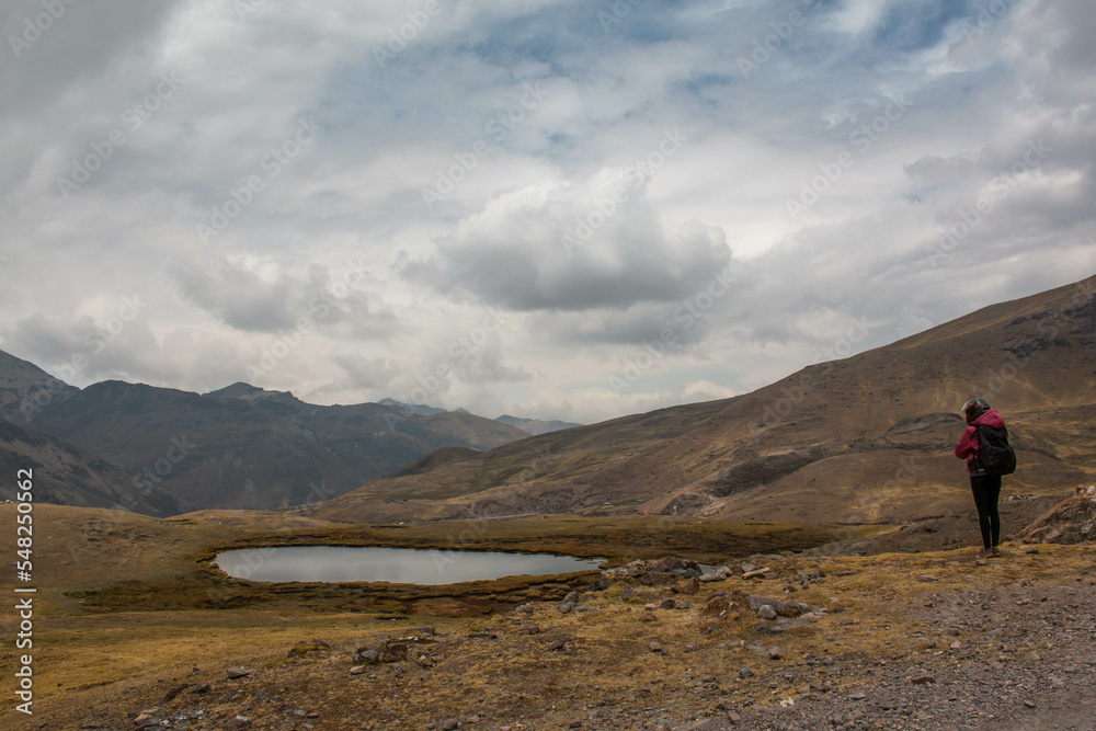 Woman with motorbike helmet next to a small rain pond, in Abra de Lares, view of the mountains and the valley, in Peru. 