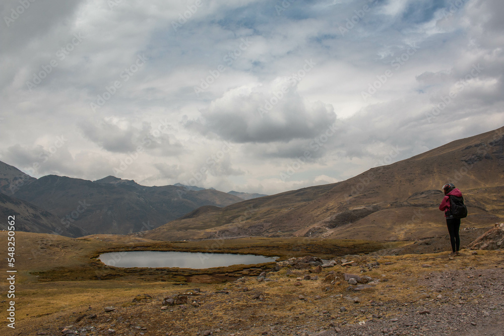 Obraz premium Woman with motorbike helmet next to a small rain pond, in Abra de Lares, view of the mountains and the valley, in Peru. 