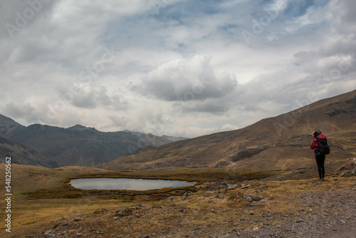 Woman with motorbike helmet next to a small rain pond, in Abra de Lares, view of the mountains and the valley, in Peru. 