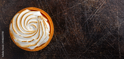 Overhead shot of a small lemon meringue tart on dark rustic background with space for text
