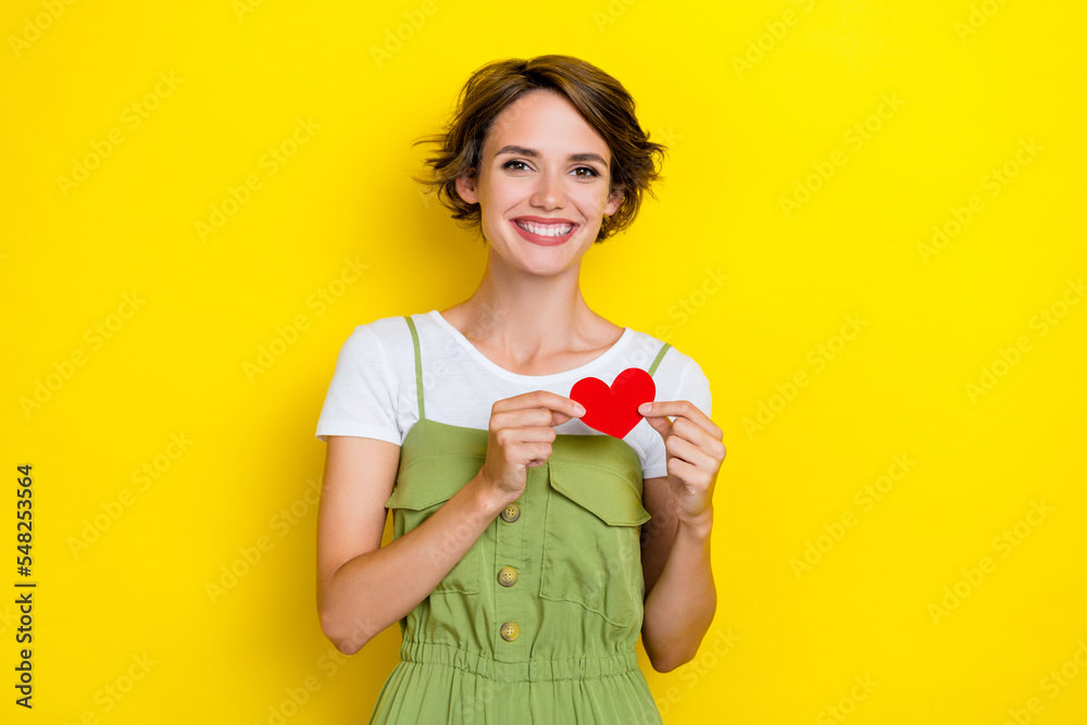 Photo of charming positive good mood lady wear khaki trendy apparel overalls hold little red paper postcard heart isolated on yellow color background Photo of charming positive good mood lady wear khaki trendy apparel overalls hold little red paper postcard heart isolated on yellow color background