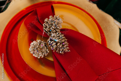 fir cones, decorated with sparkles and plastic rhinestones, lie on a red napkin on a yellow plate, background in blur
