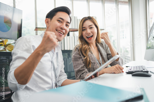 Excited young Asian startup business team celebrate successful and victory and hand up at office and looking at camera, happy euphoric proud Asian male and female professional winner feel overjoyed