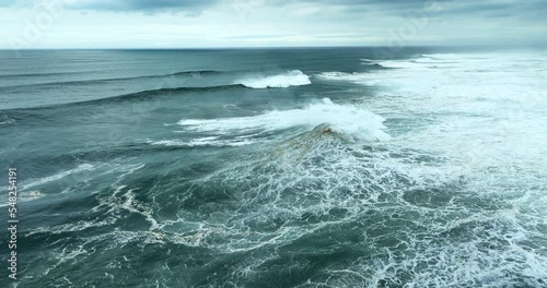 Aerial view of powerful dark ocean waves rolling from above. Drone flying over fabulous sea tide on a stormy day. Breaking surf with foam in Atlantic ocean. Big swell in Nazare, Portugal.