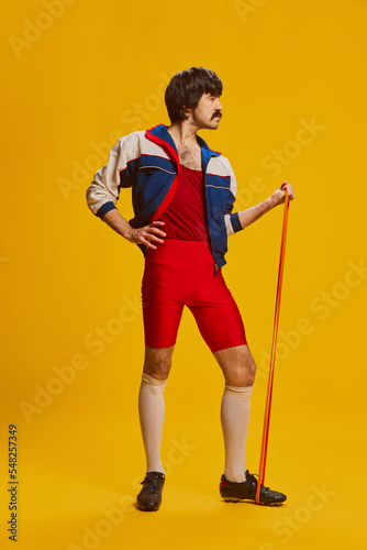 Portrait of stylish man with moustache posing in vintage sportswear with sports expander isolated over yellow background. Funny face