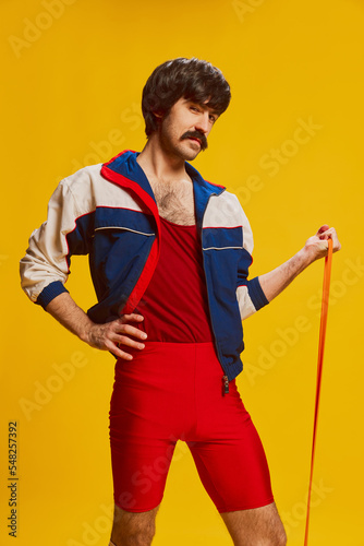 Portrait of stylish man with moustache posing in vintage sportswear with sports expander isolated over yellow background. Sportive life