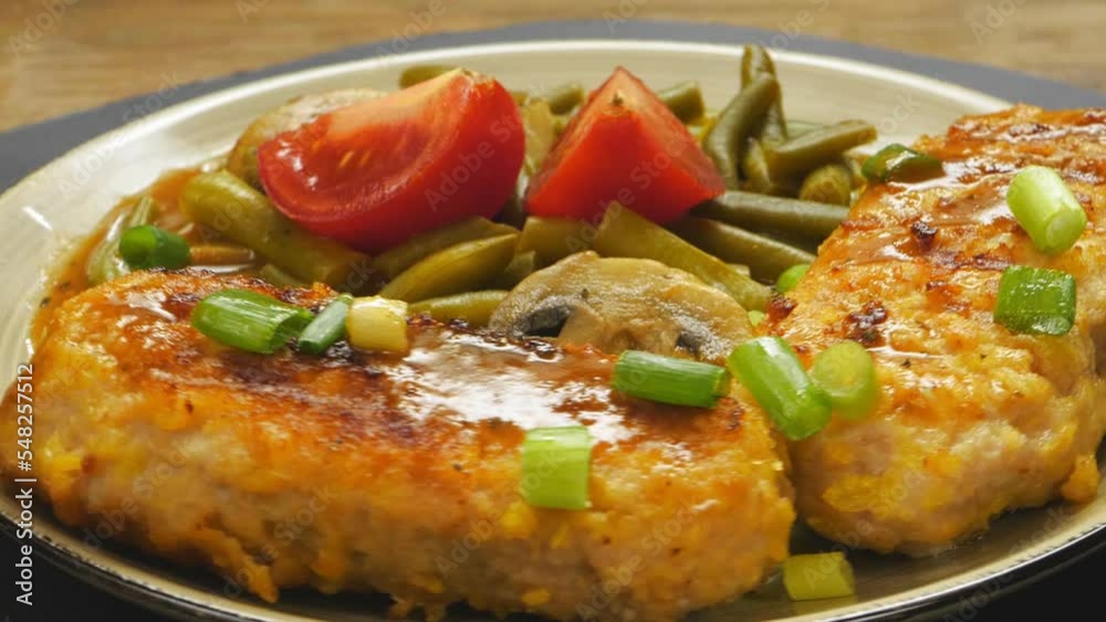 Chopped meat cutlets with green beans and champignons in tomato sauce garnished with green tomatoes in a plate rotates in a circle. Close-up. Chopped meat cutlets with green beans and champignons in tomato sauce garnished with green tomatoes in a plate rotates in a circle. Close-up.
