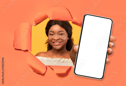 Pretty african american woman looking through torn in orange wall © Prostock-studio