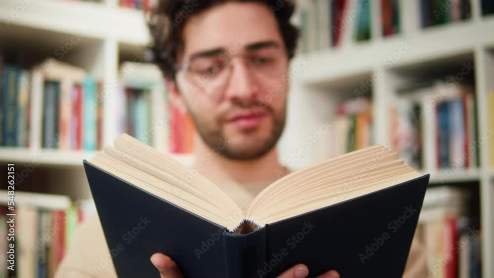 Man reading Book in University Library, Book Shop or Store, Spanish Student Wearing Glasses Standing near Bookshelf Reads Book and Exam Preparations. Man reading Book in University Library, Book Shop or Store, Spanish Student Wearing Glasses Standing near Bookshelf Reads Book and Exam Preparations.